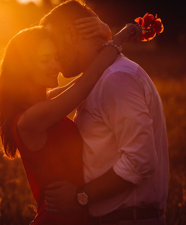 Handsome bearded man hugs woman in red dress tender standing in golden summer field